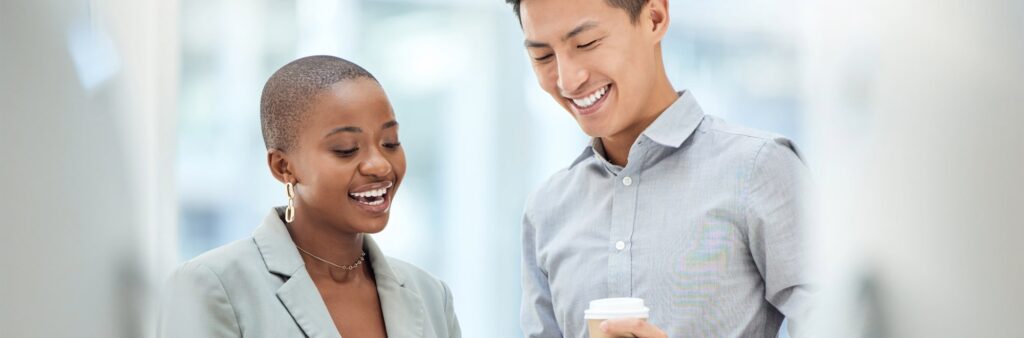 A male and female colleagues looking down at a tablet and smiling