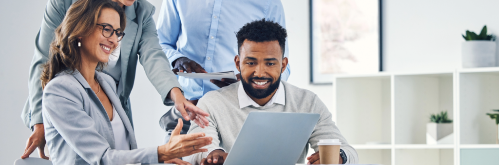 A group of colleagues smiling around a laptop communicating and building accountability within the organization.