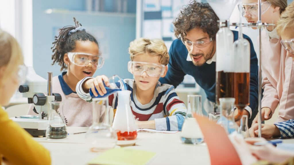 Teacher helping young students with a science experiment so they can meet an audacious goal.