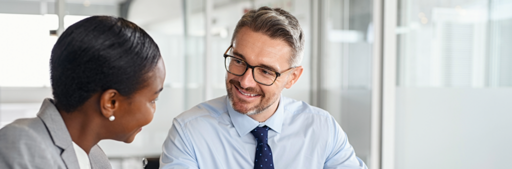 Man smiling at a woman in an office; they are deep in conversation. One is giving constructive feedback to another