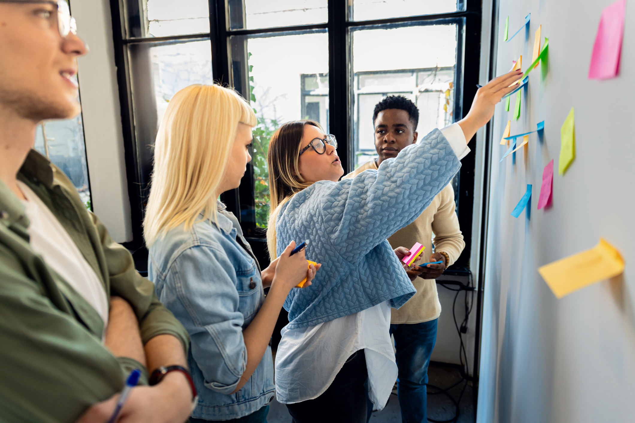Diverse group of young business people working in office using colorful sticky notes on wall to organize their ideas.