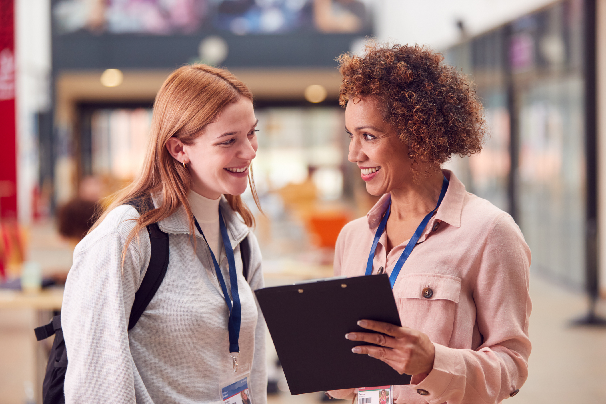 Female College Student Meeting With Woman Tutor In Busy Communal Campus Building
